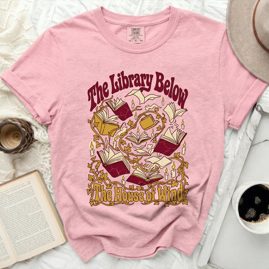 Pink t-shirt with "The Library Below The House of Wind" text and book graphics.