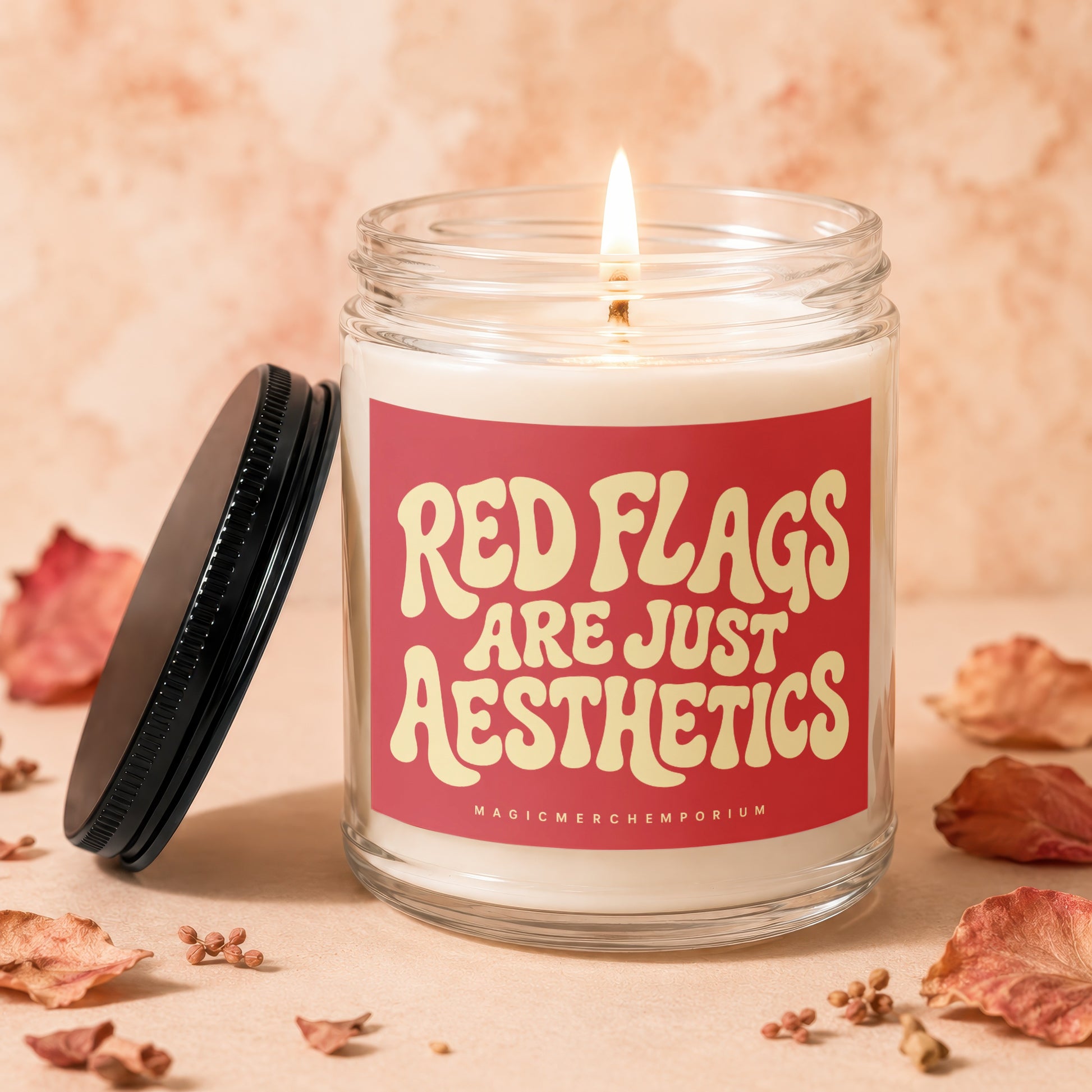 Glass jar candle with lit wick and red label saying "Red Flags Are Just Aesthetics".