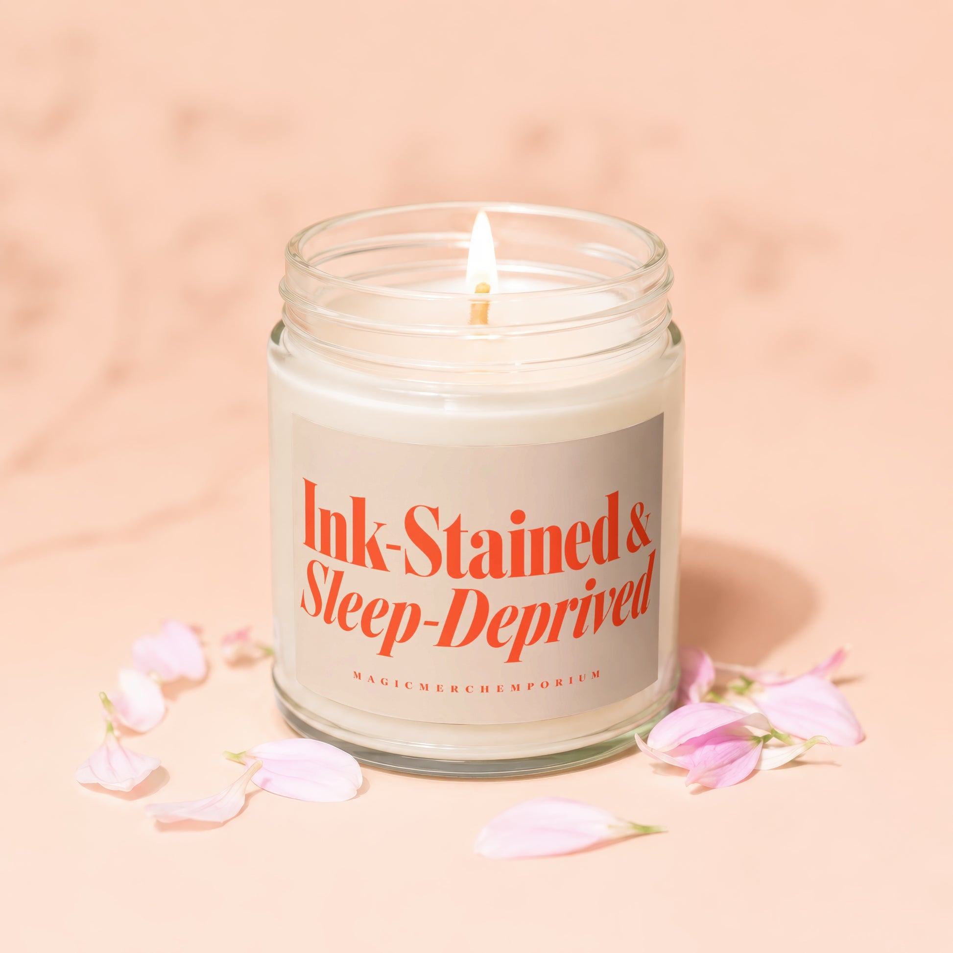 Jar candle with "Ink-Stained & Sleep-Deprived" text, surrounded by pink petals.