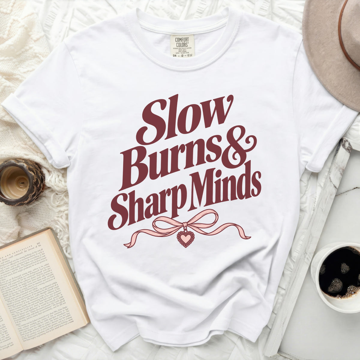 White t-shirt with burgundy text "Slow Burns & Sharp Minds" and a pink bow.