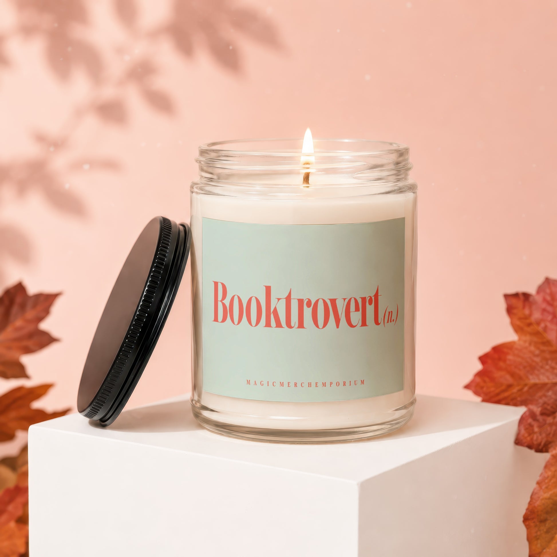 Glass candle with lit wick, "Booktrovert" label, and black lid.
