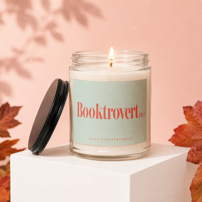 Glass candle with lit wick, "Booktrovert" label, and black lid.