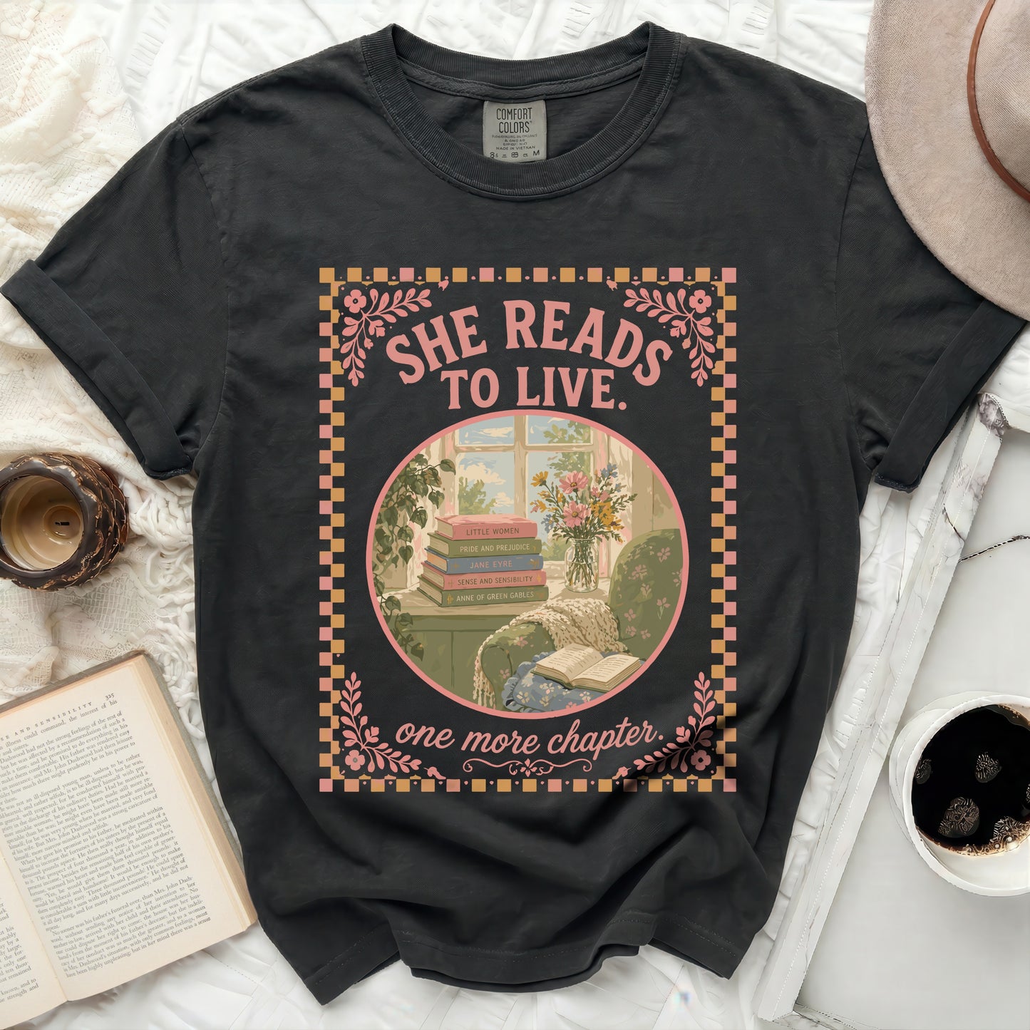 Black t-shirt with "SHE READS TO LIVE. one more chapter." text and book illustrations.