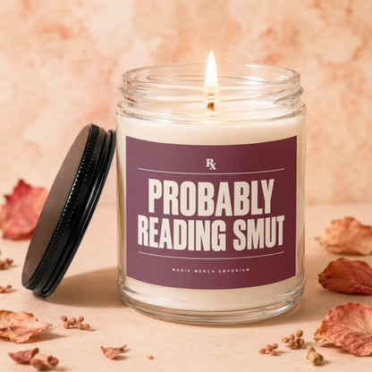 Lit glass jar candle with label that reads "PROBABLY READING SMUT" and "MAGIC MERCH EMPORIUM".