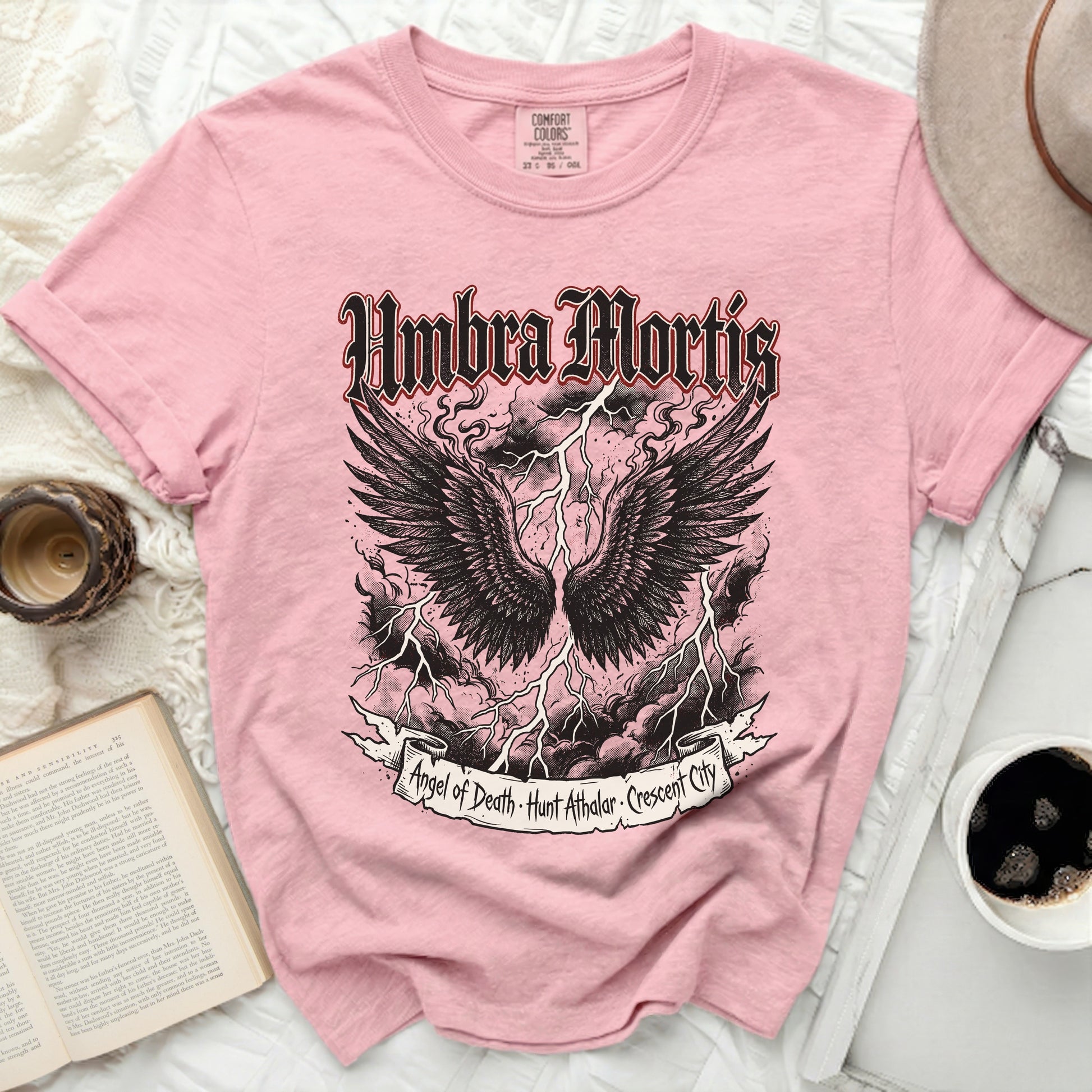 Pink t-shirt with black winged skull graphic and "Umbra Mortis" text.