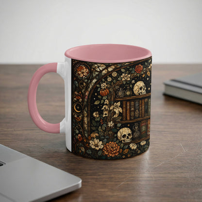 Mug with pink handle featuring a dark, stained-glass style illustration of a bookshelf with skulls and flowers.