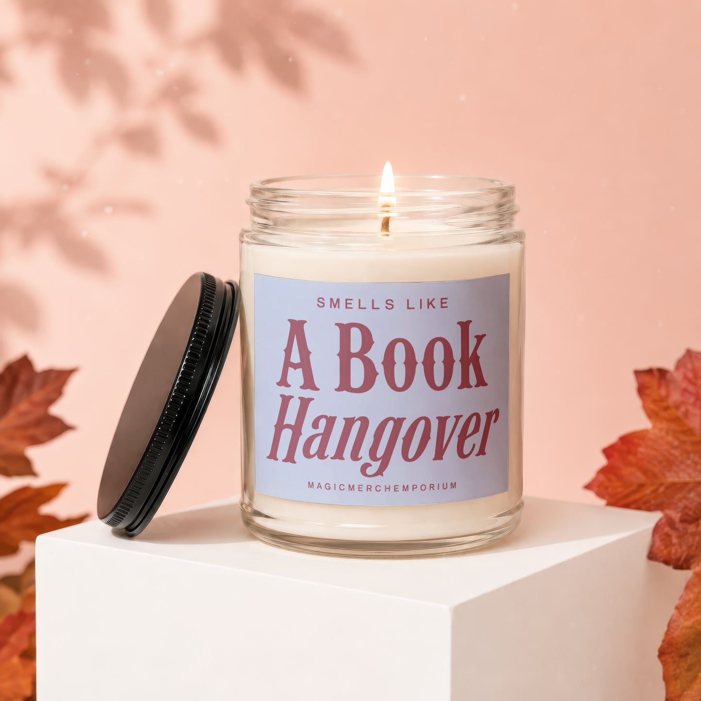 Lit candle in glass jar with "Smells Like A Book Hangover" label and black lid.