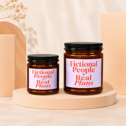 Two amber glass candles with black lids, labeled "Fictional People Real Plans".