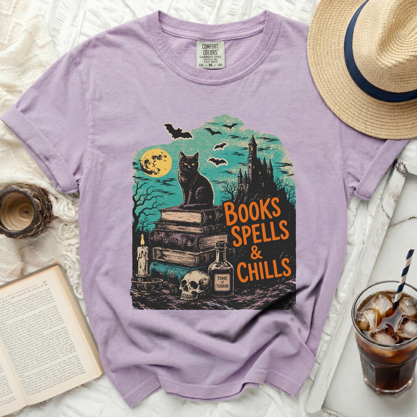 Lavender comfort colors shirt with Halloween graphic of black cat, books, and castle.