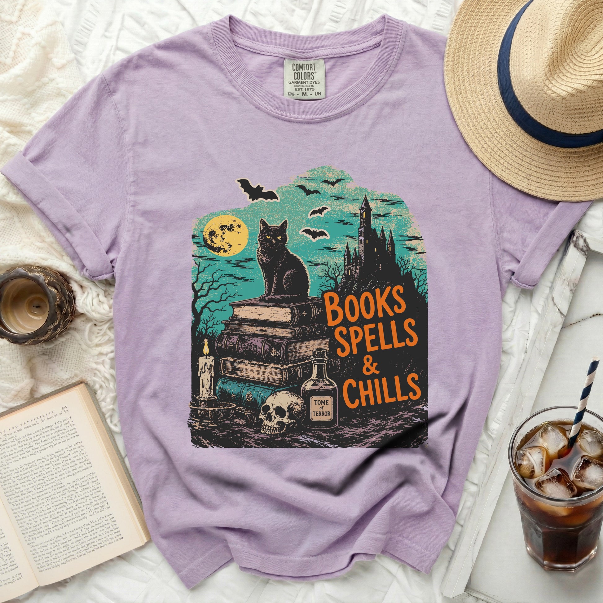 Lavender comfort colors shirt with Halloween graphic of black cat, books, and castle.