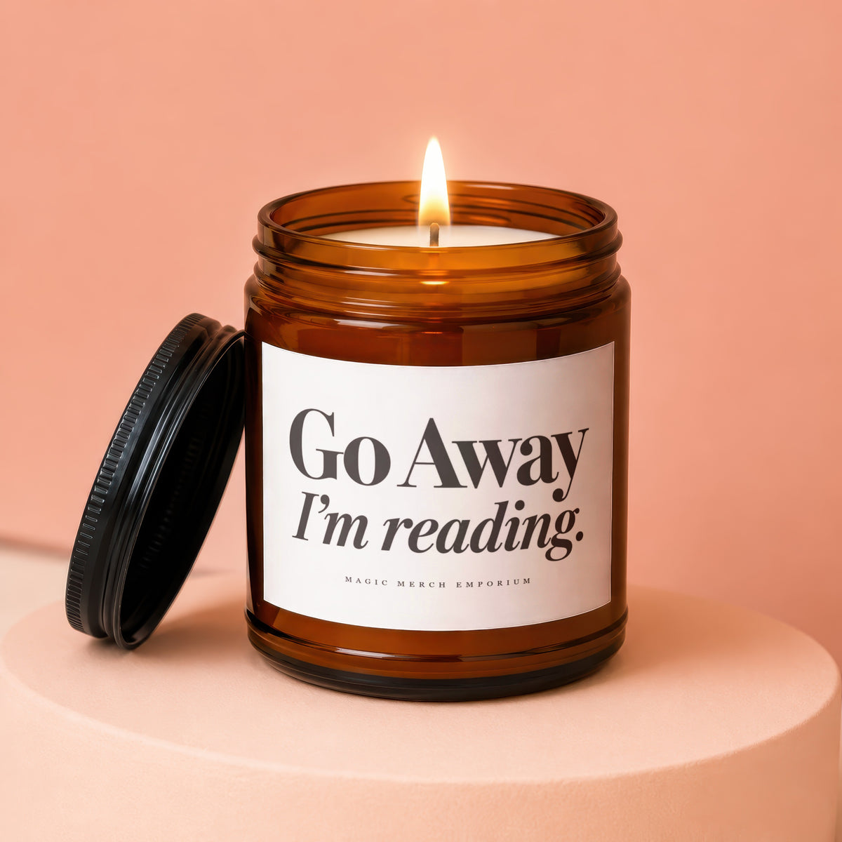 Amber jar candle with lit flame, reading "Go Away I'm reading."