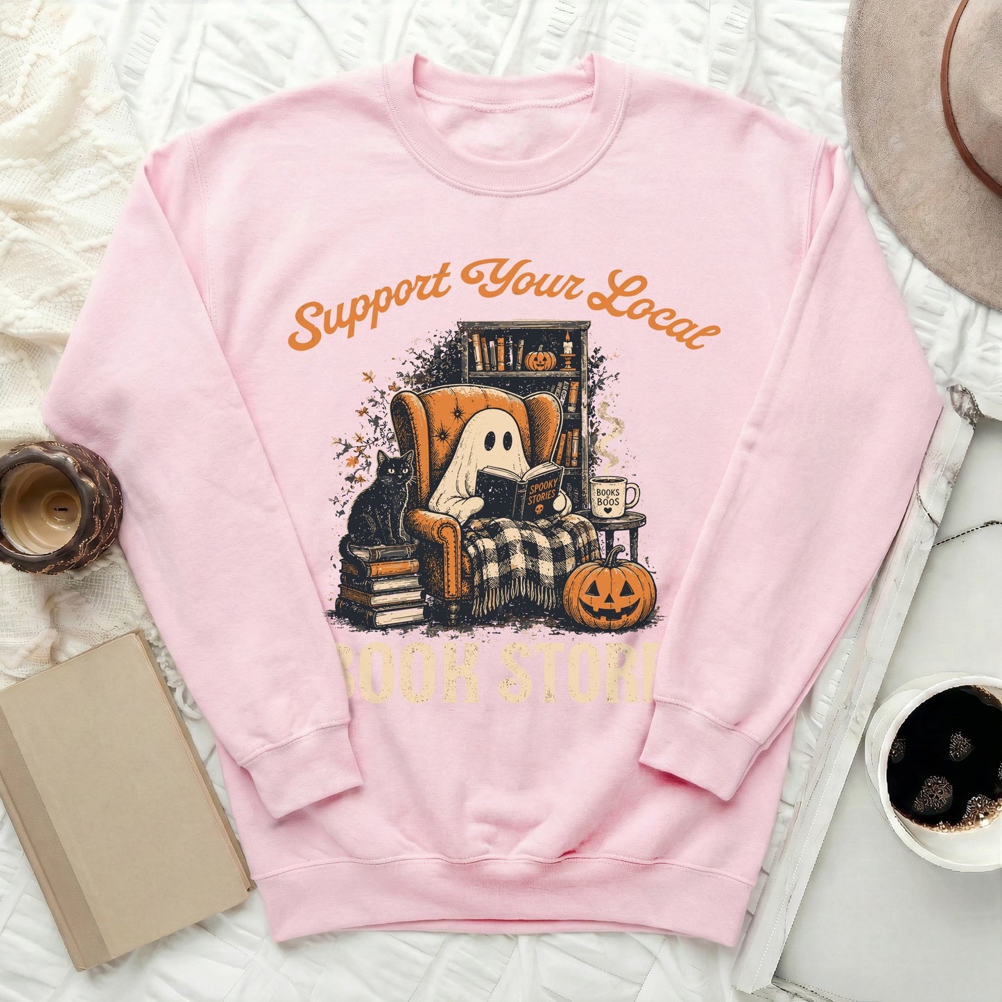 Pink sweatshirt with illustration of ghost reading "Spooky Stories" in armchair with cat.