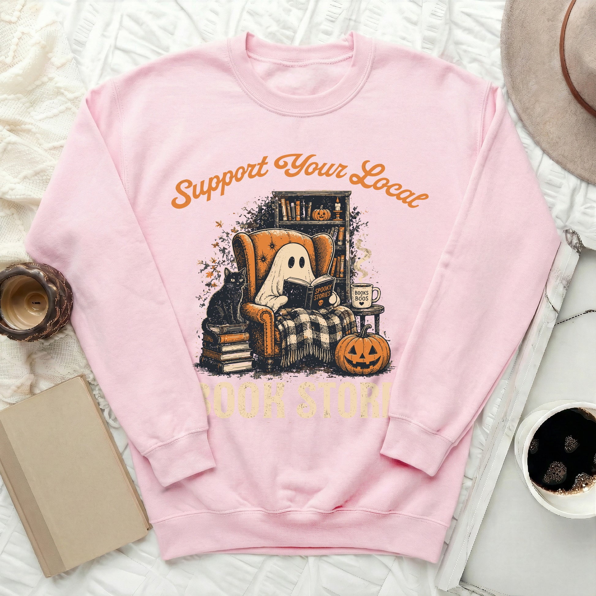 Pink sweatshirt with illustration of ghost reading "Spooky Stories" in armchair with cat.