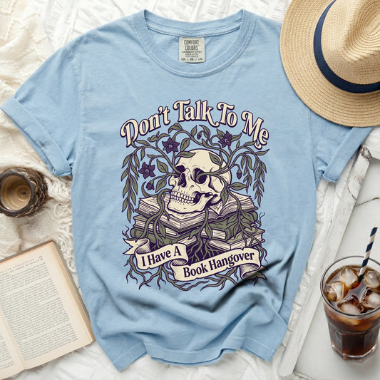 Light blue t-shirt with skull, books, vines, and "I Have a Book Hangover" text.