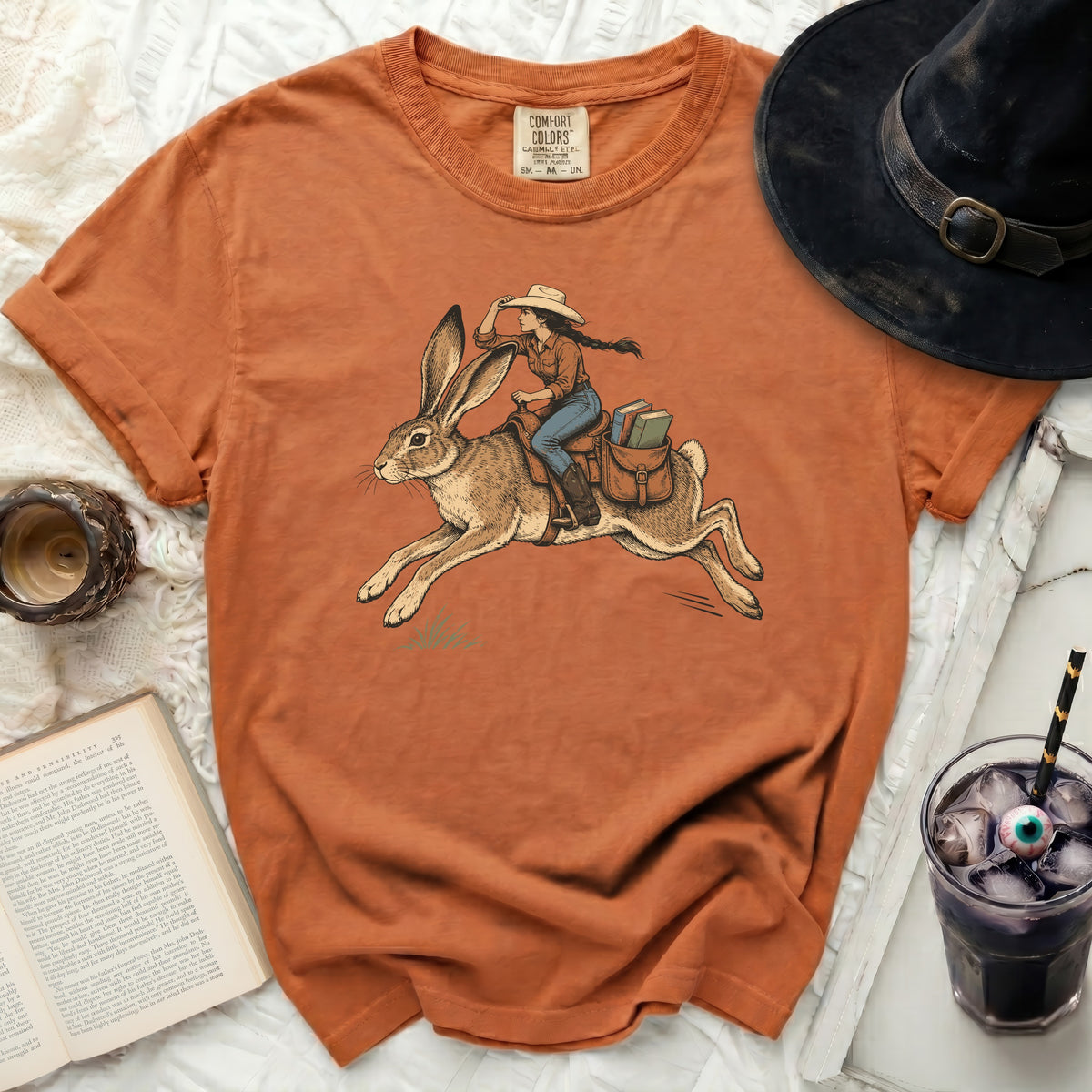 Orange t-shirt with graphic of woman riding a rabbit, carrying books.