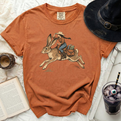 Orange t-shirt with graphic of woman riding a rabbit, carrying books.