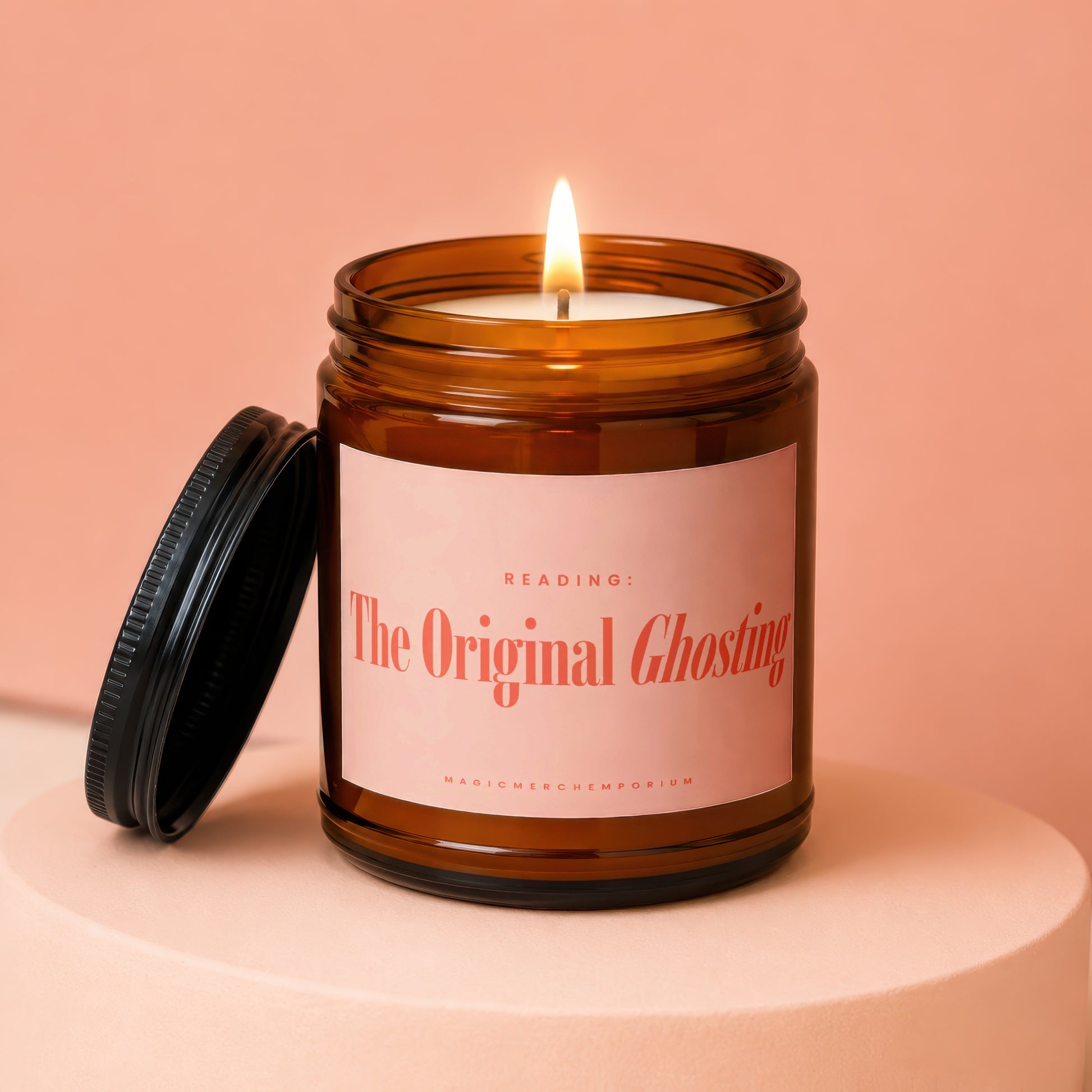 Amber jar candle with lit wick and black lid. Label reads "READING: The Original Ghosting".