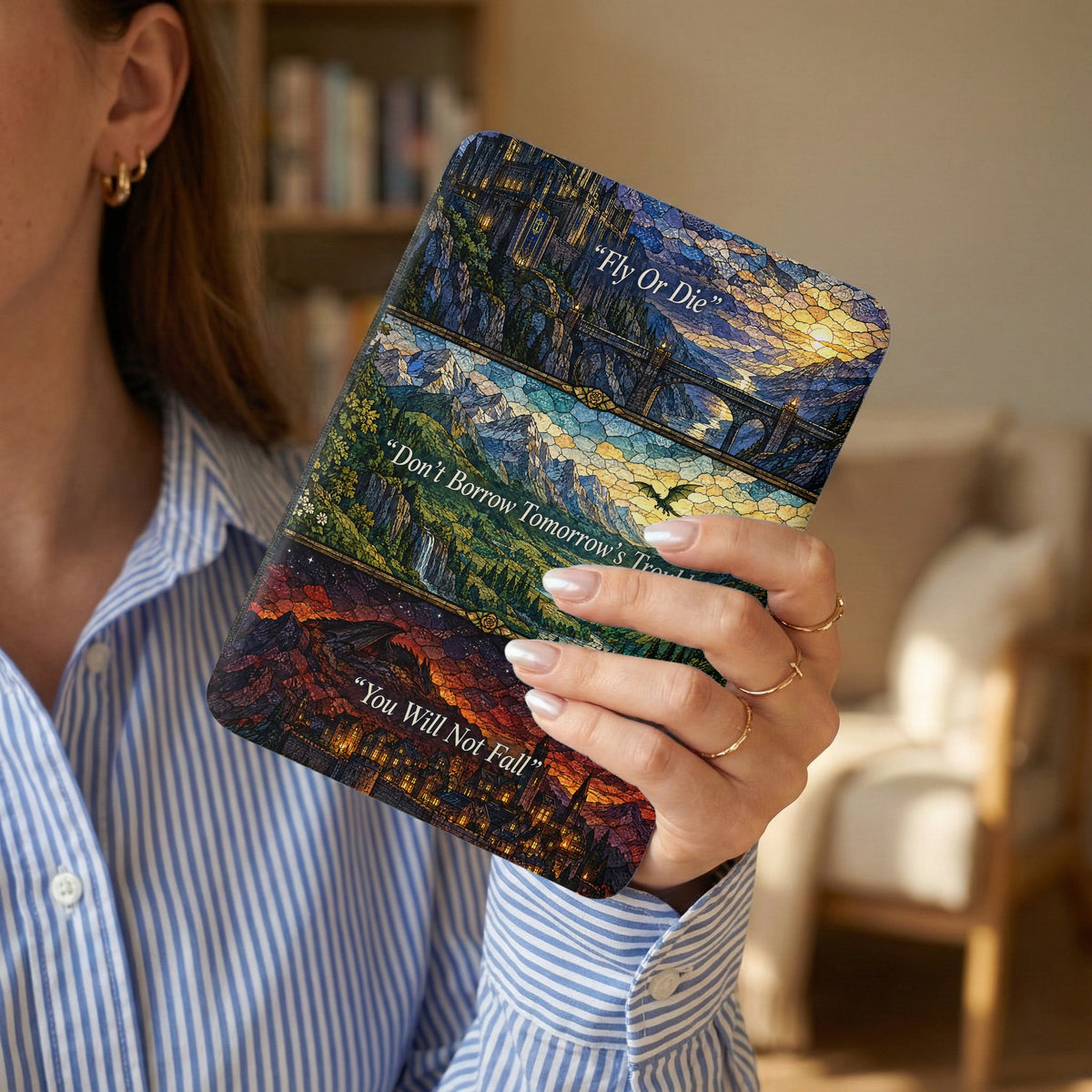 A person holds a Kindle with a stained glass-style fantasy landscape case featuring inspirational quotes.
