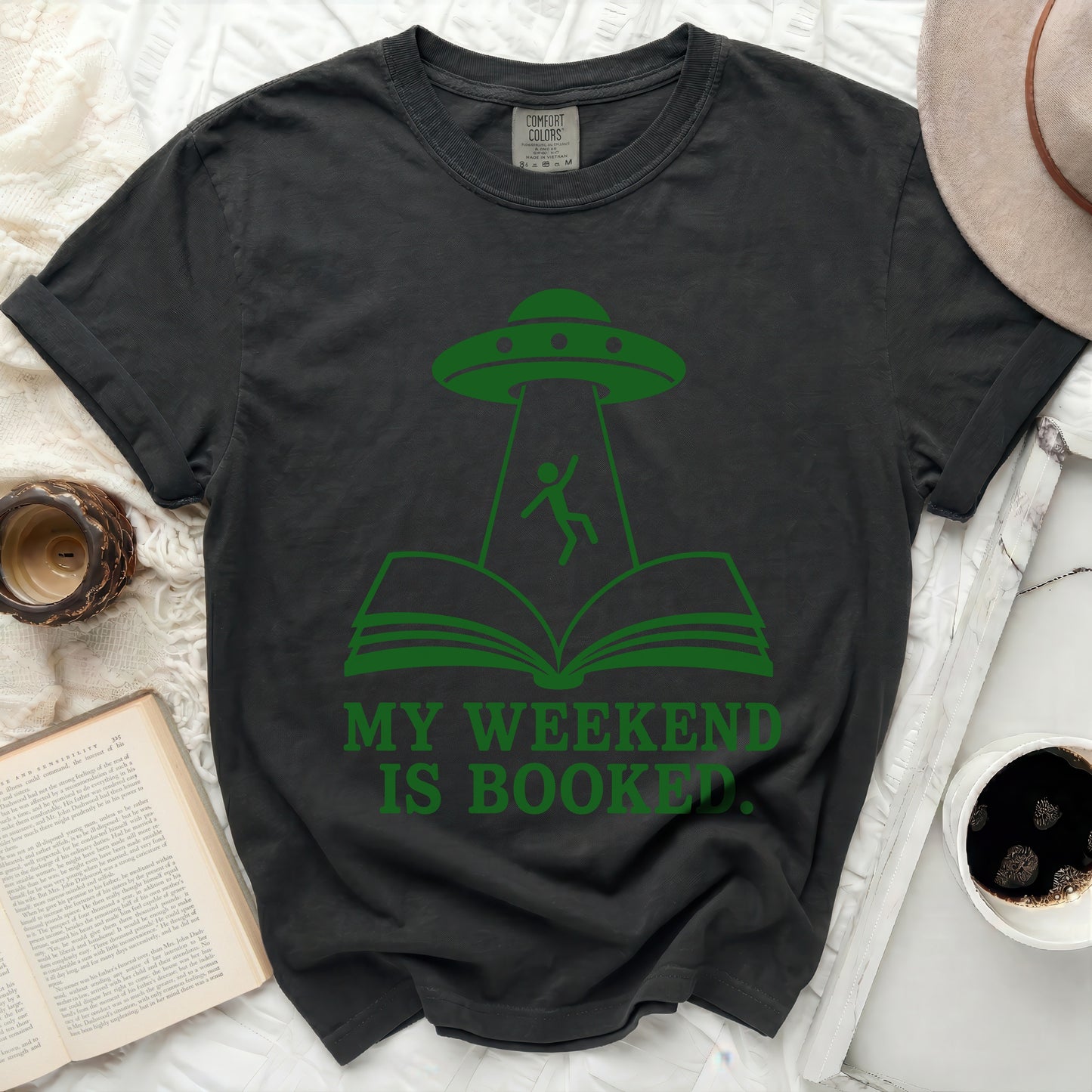 Dark t-shirt with green alien abduction and open book graphic, "MY WEEKEND IS BOOKED."