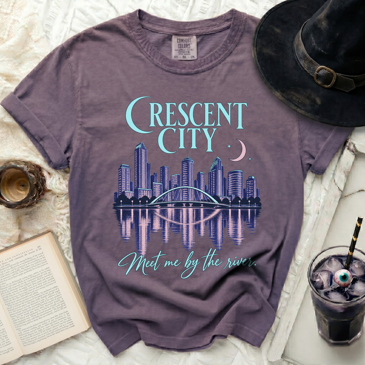 Purple t-shirt with "Crescent City" skyline graphic and "Meet me by the river" text.