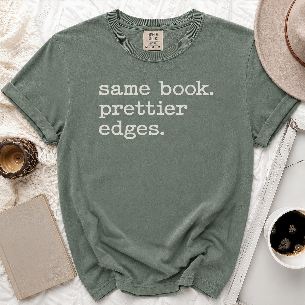 T-shirt with "Same book. Prettier edges." text, laid flat with book and hat.