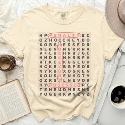 Cream t-shirt with word search spelling "penalty," "hockey," and "obsessed."