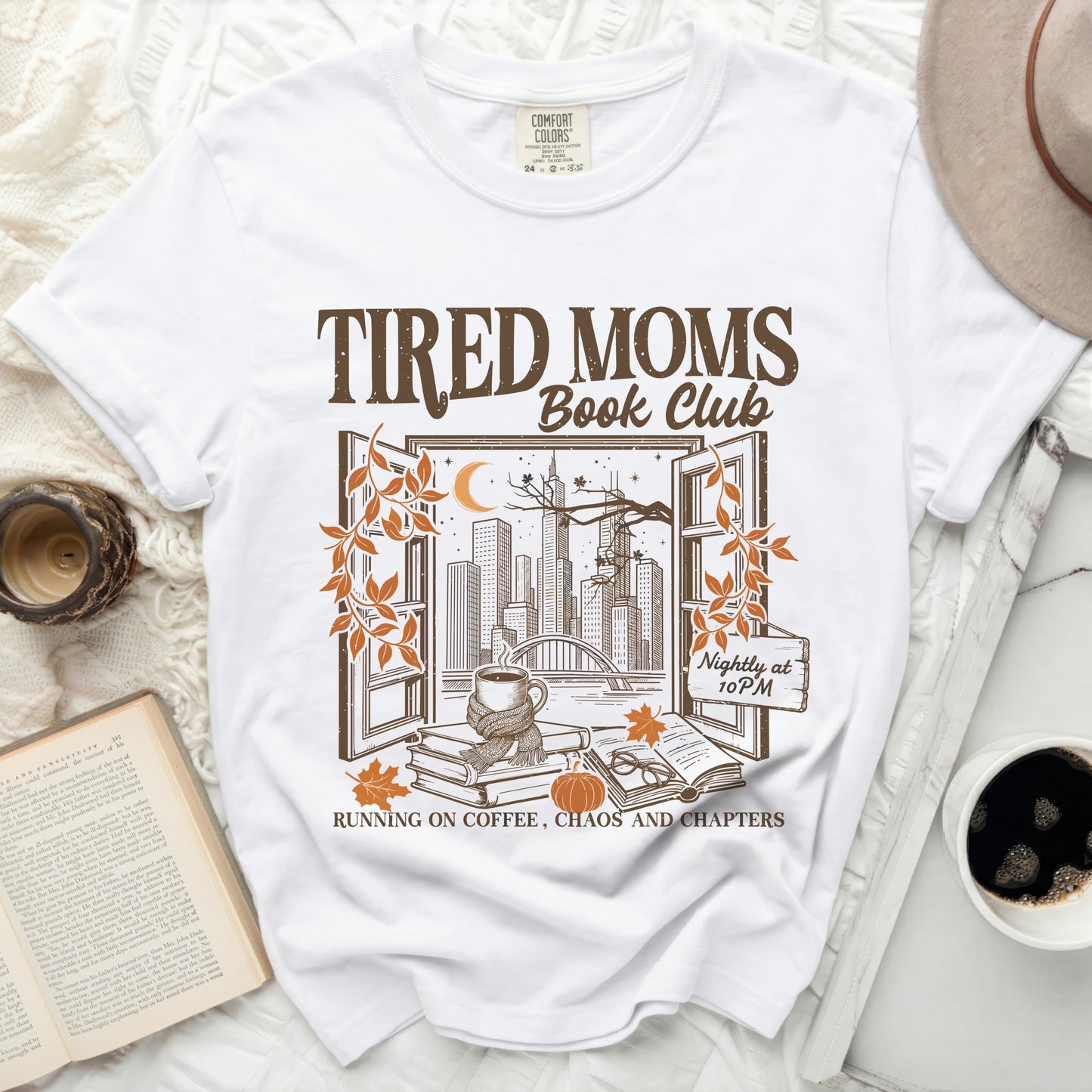 White t-shirt graphic with "Tired Moms Book Club" text and city view.