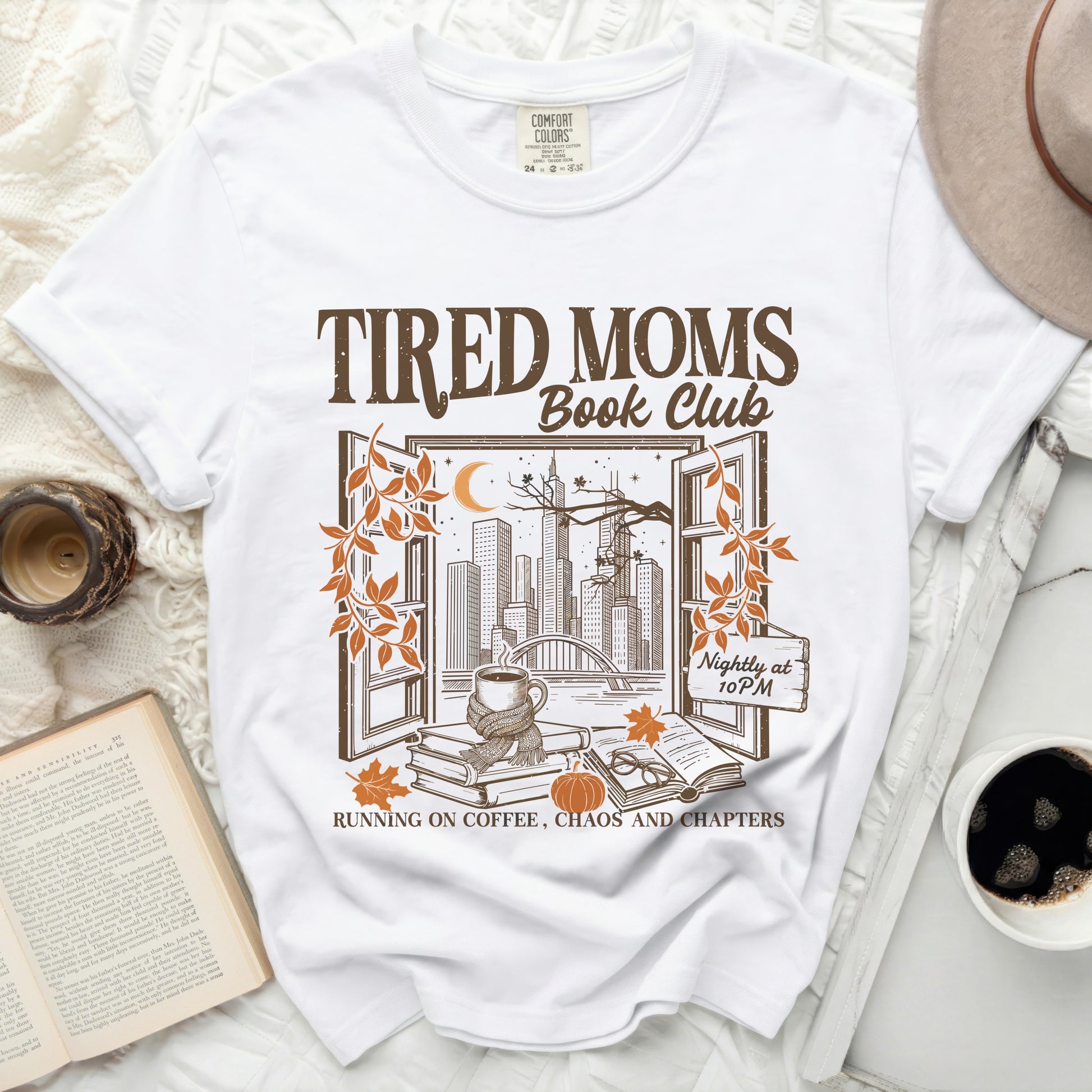 White t-shirt graphic with "Tired Moms Book Club" text and city view.