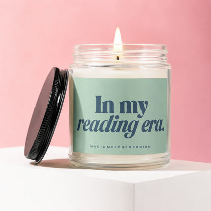 Candle with lit wick and black lid, reading "In my reading era. MAGICMERCHƐMPORIUM"