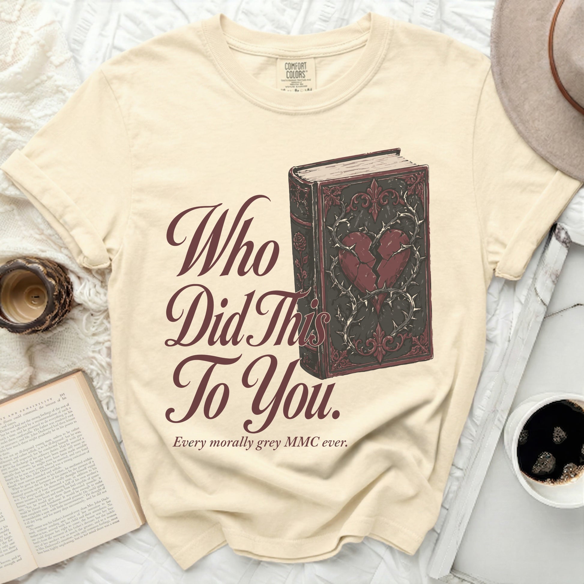 Cream t-shirt with a book graphic and "Who Did This To You." text.