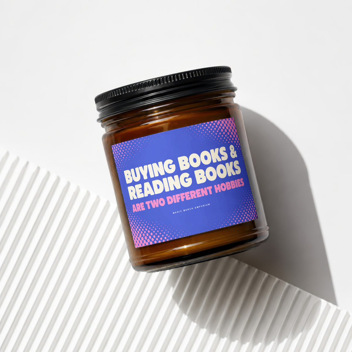 Amber jar candle with a blue label reading "Buying Books & Reading Books Are Two Different Hobbies".