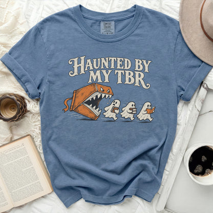Blue t-shirt with "Haunted by My TBR" graphic of a book monster chasing ghosts reading books.
