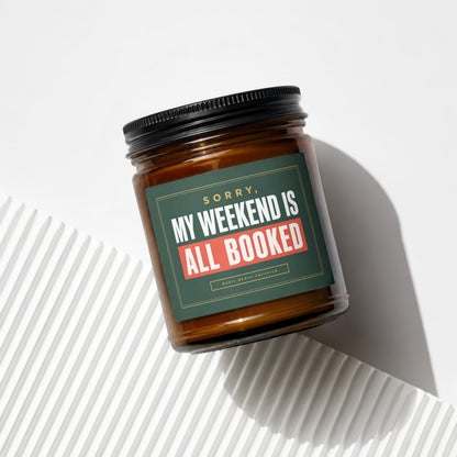 Amber jar candle with a green label that reads "Sorry, My Weekend Is All Booked."