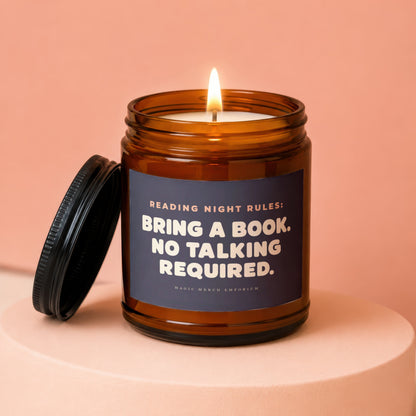 Amber candle with lit wick and lid off, reading "Bring a book. No talking required."