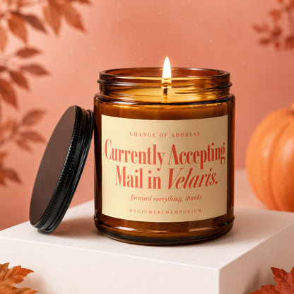 A lit amber candle with a black lid and a custom label reading Currently Accepting Mail in Velaris.