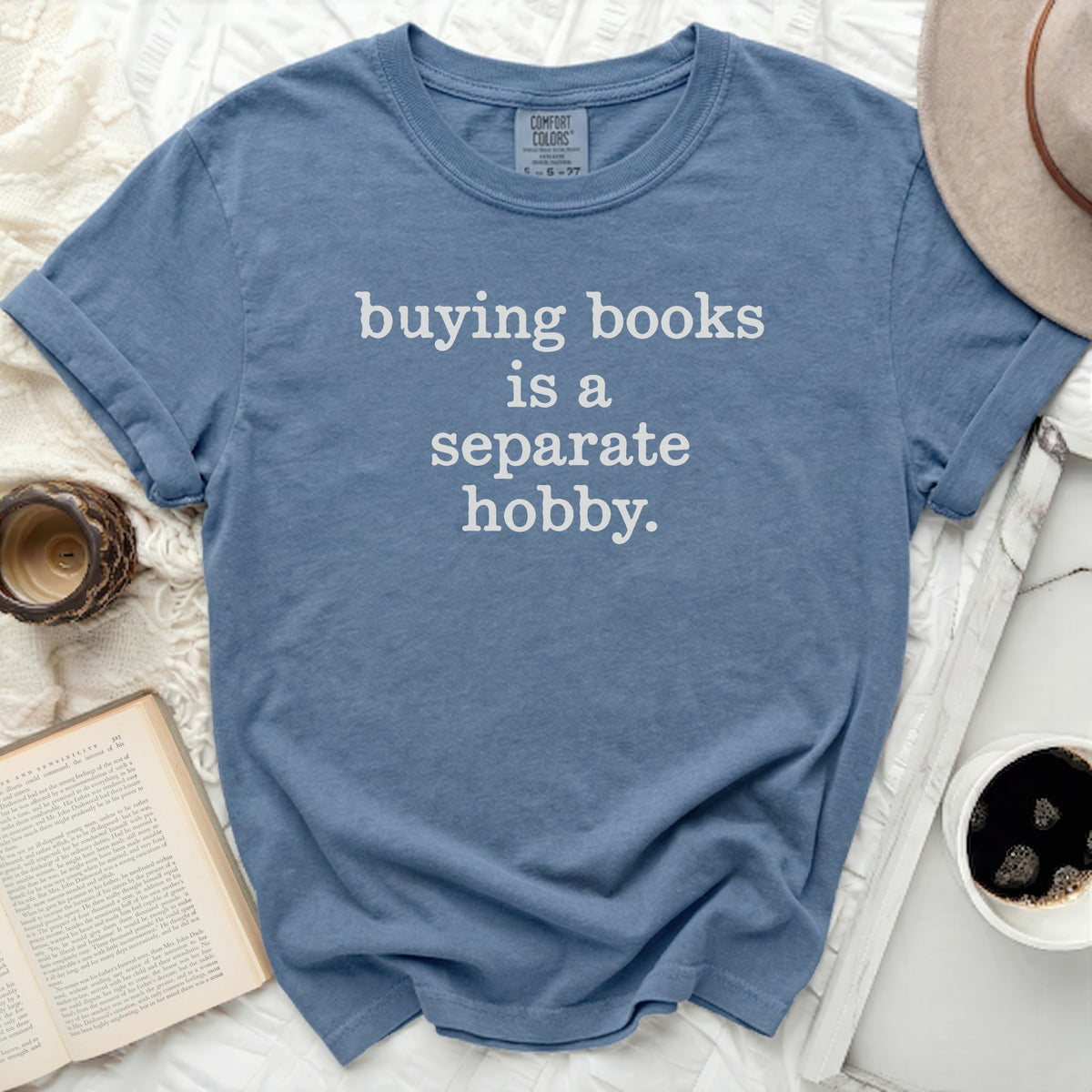 Blue t-shirt with white text "buying books is a separate hobby."