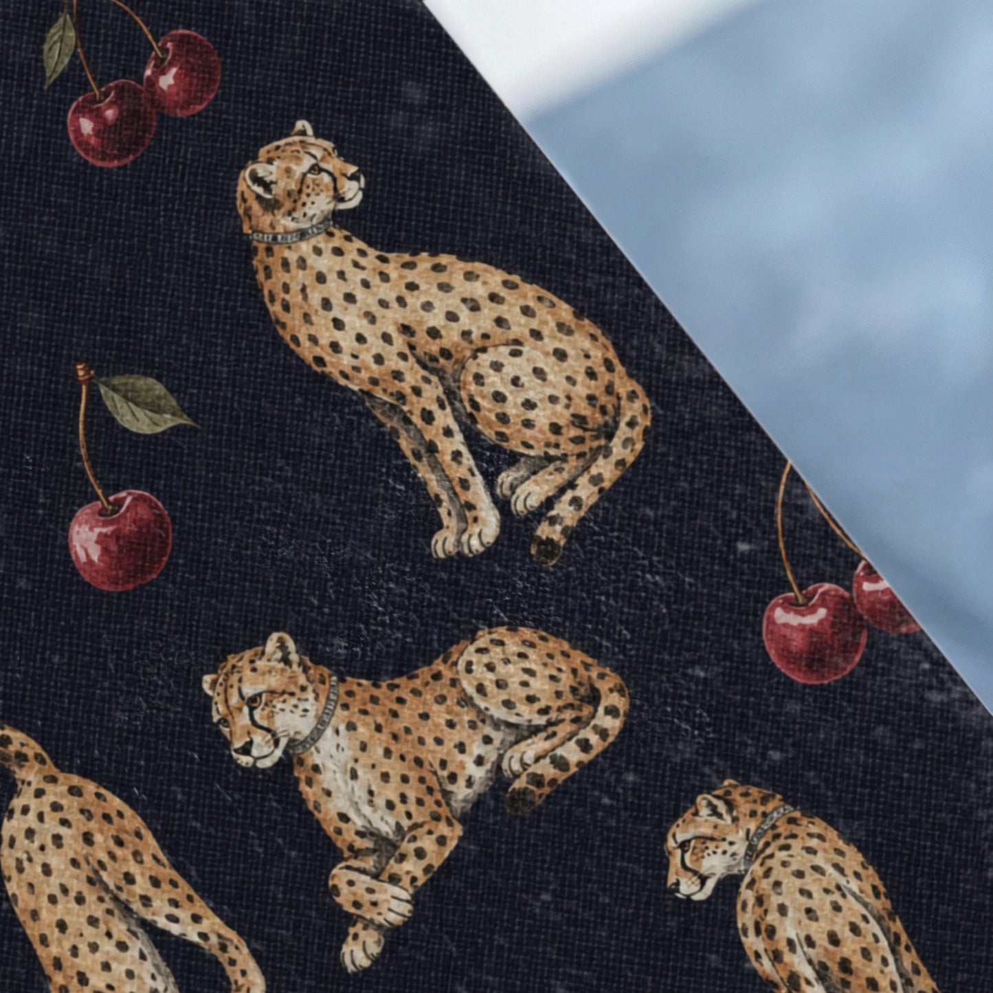 Dark blue fabric with a pattern of cheetahs and cherries, against a light blue background.