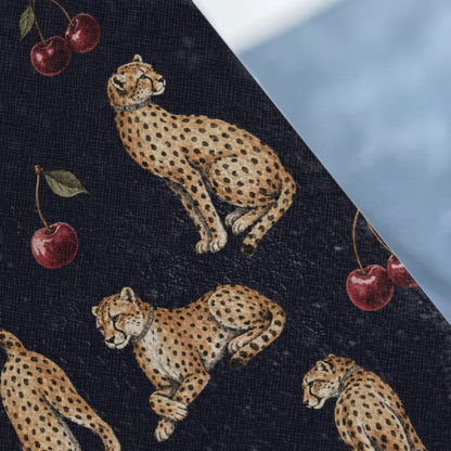 Dark blue fabric with a pattern of cheetahs and cherries, against a light blue background.