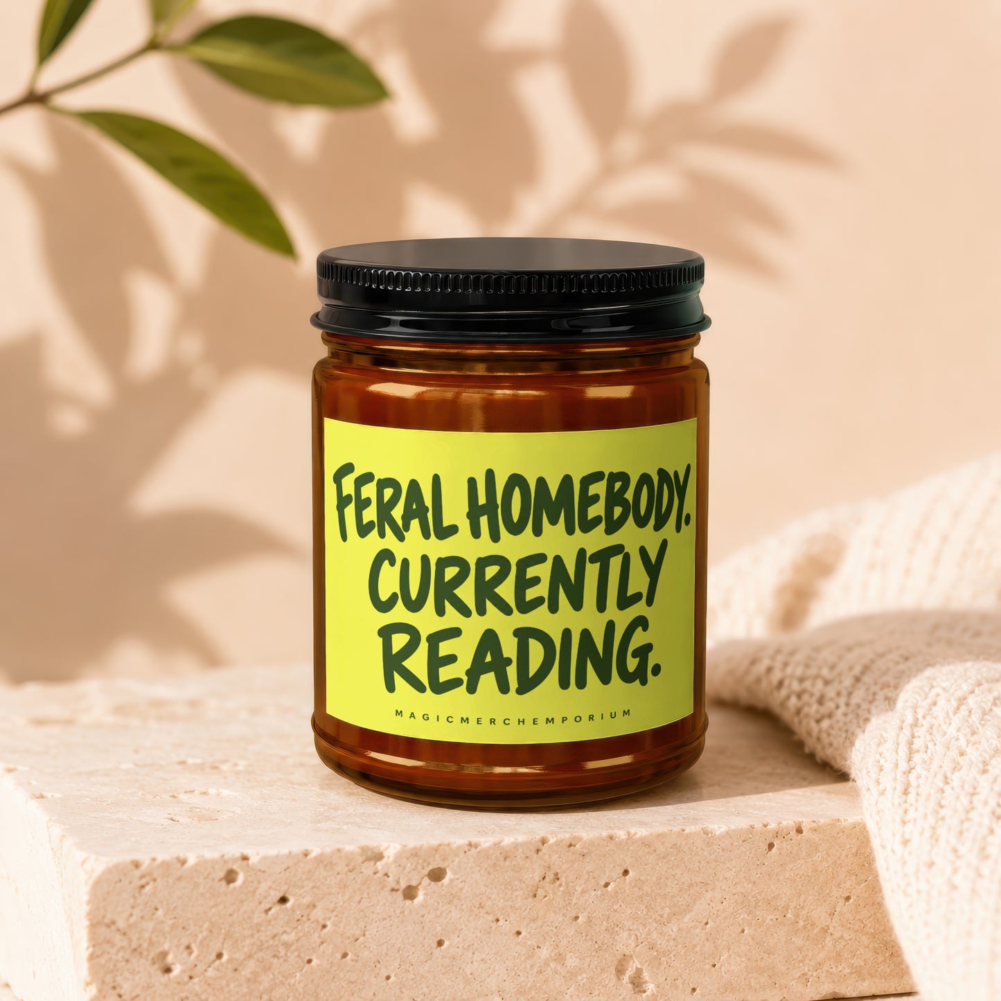Brown glass candle with yellow label saying "Feral Homebody Currently Reading."