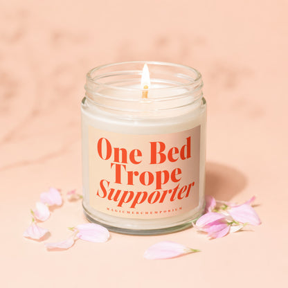 Lit candle with orange text on label reading "One Bed Trope Supporter"