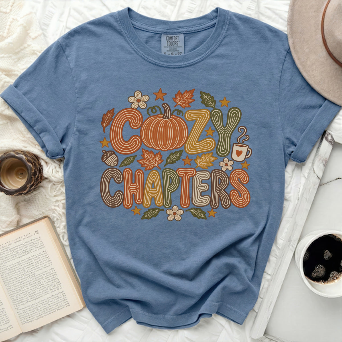Blue t-shirt with "Cozy Chapters" graphic featuring a pumpkin, leaves, and flowers.