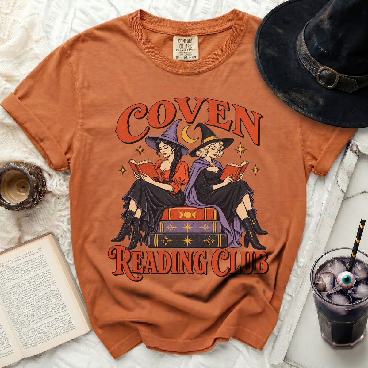 Orange t-shirt with "Coven Reading Club" graphic of witches reading books.