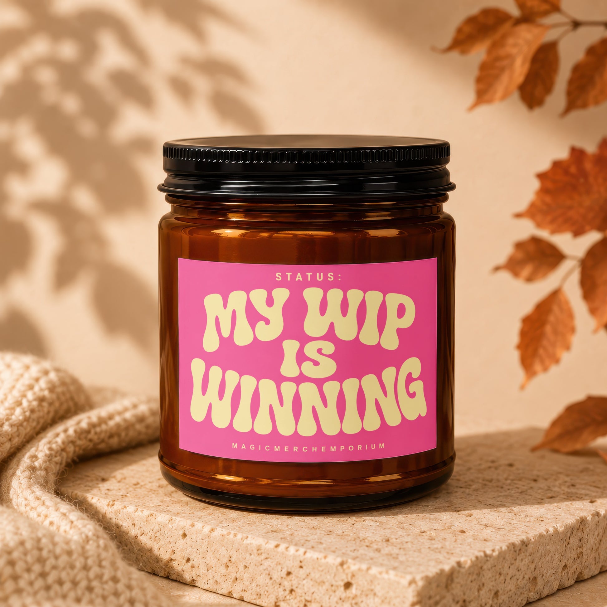 Amber candle with pink label reading "Status: My WIP is Winning".