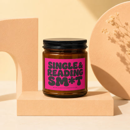 Amber jar candle with pink label that reads "SINGLE & READING SM*T".