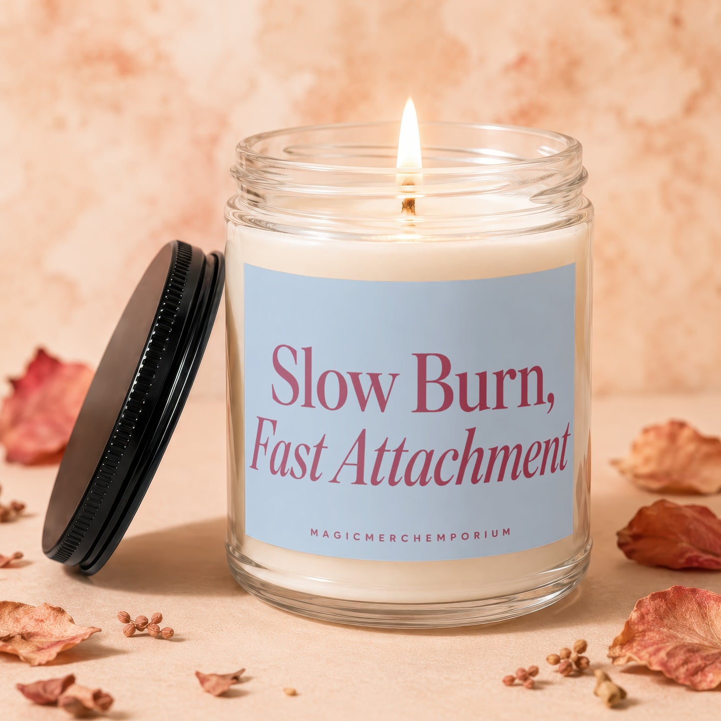 Glass jar candle, lit flame, "Slow Burn, Fast Attachment" text, and dried petals.