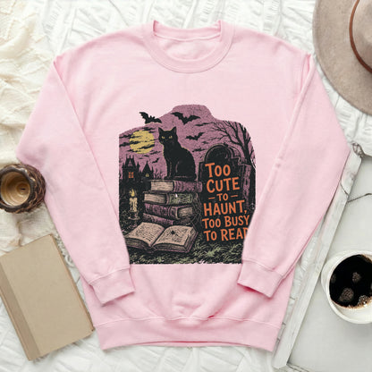 Pink sweatshirt with a graphic of a black cat on books, text reads "Too Cute to Haunt".