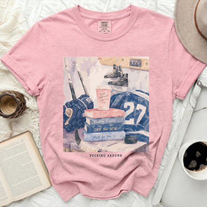 Pink t-shirt with hockey gear, books, and coffee cup, "Pucking Around" text.