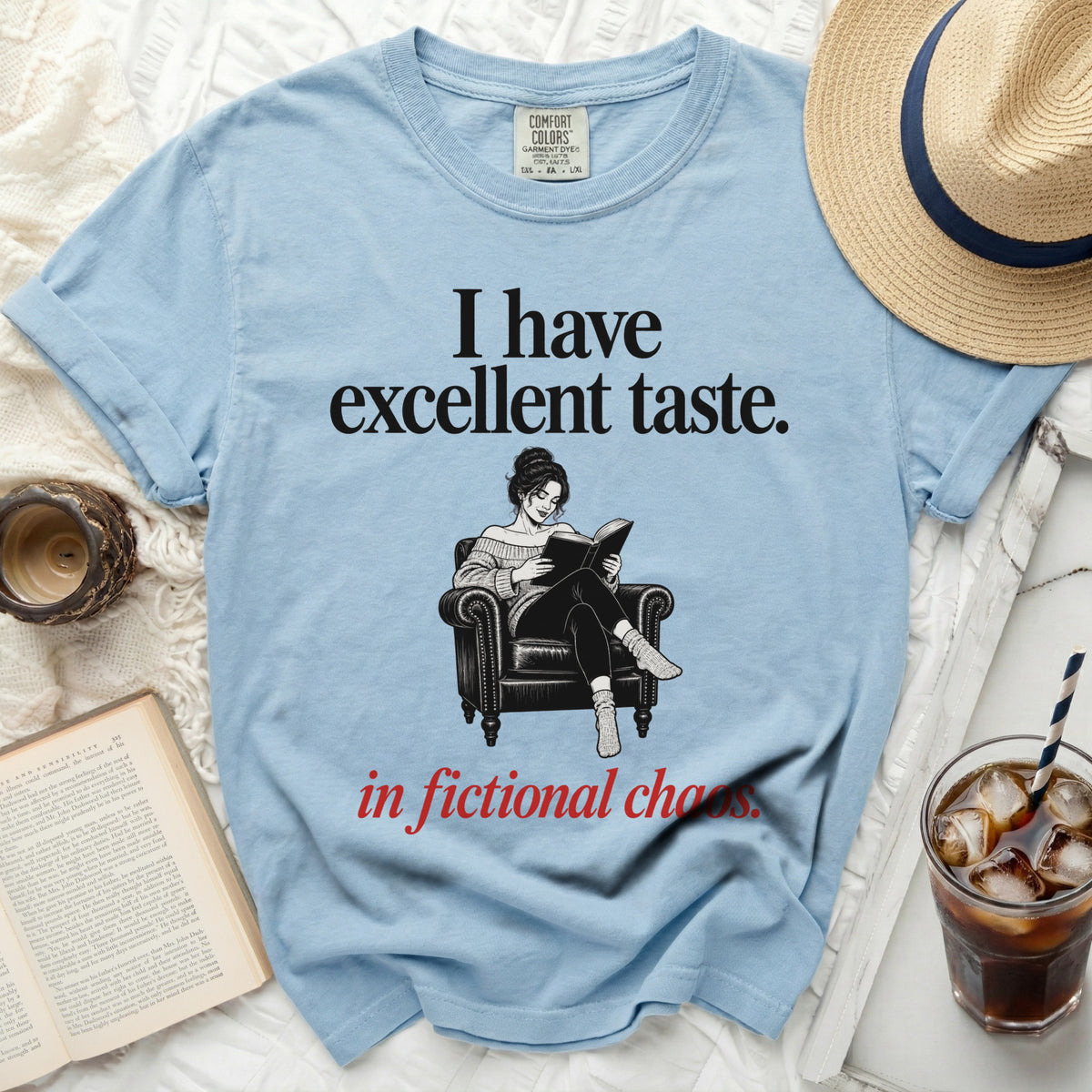 Light blue t-shirt with "I have excellent taste." and "in fictional chaos." text and reading woman graphic.