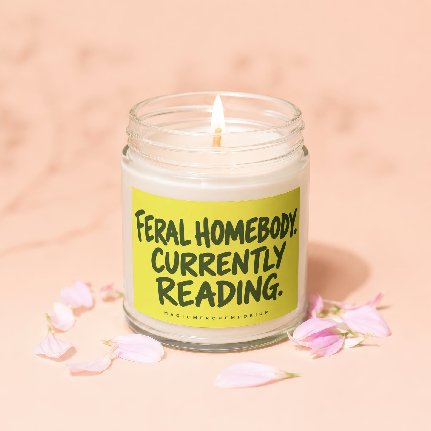 Glass jar candle with lit wick and a lime green label reading "Feral Homebody Currently Reading."