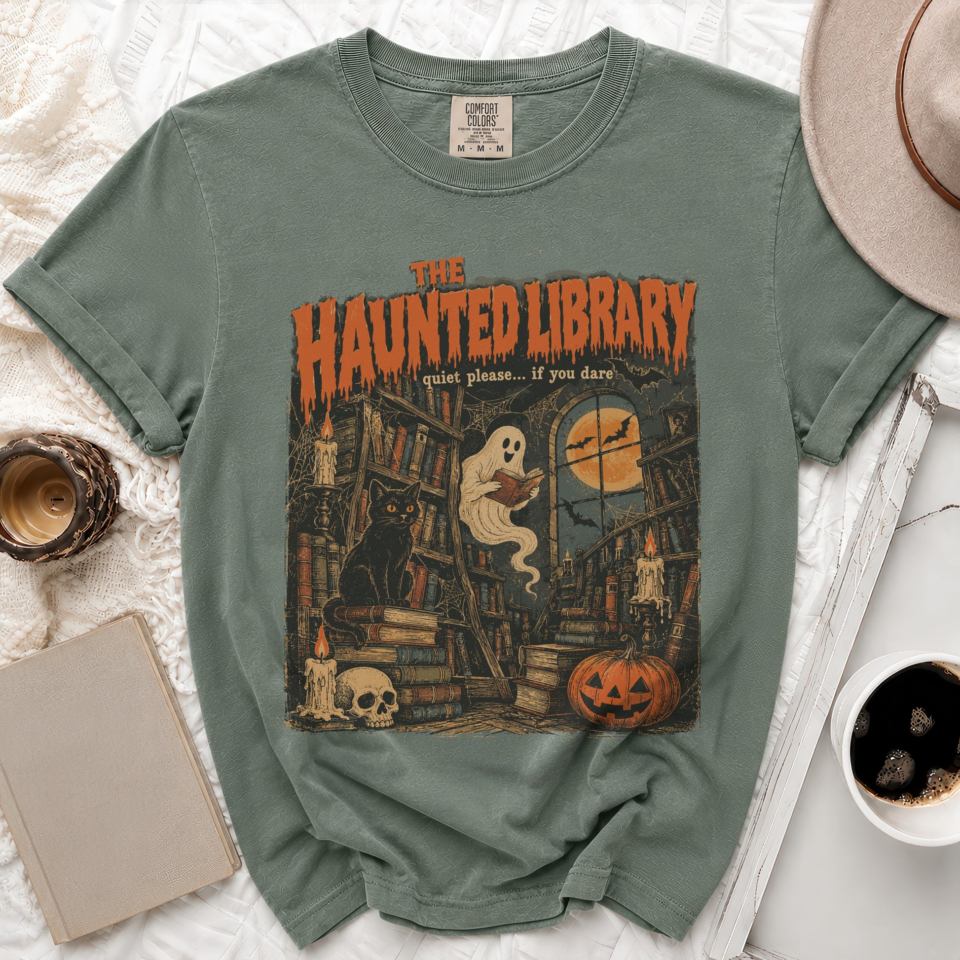 Green t-shirt graphic of "The Haunted Library" with ghost, cat, and Halloween elements.